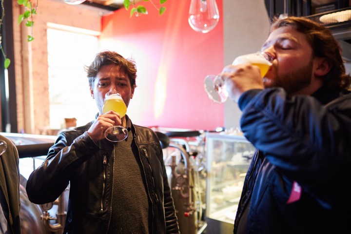 Two people drinking beer in a brewery with bright lighting.