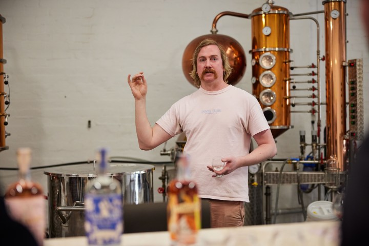 Person speaking in a distillery with copper equipment in the background.