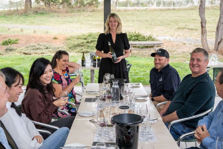Group of people enjoying wine at an outdoor table with a server standing and smiling.