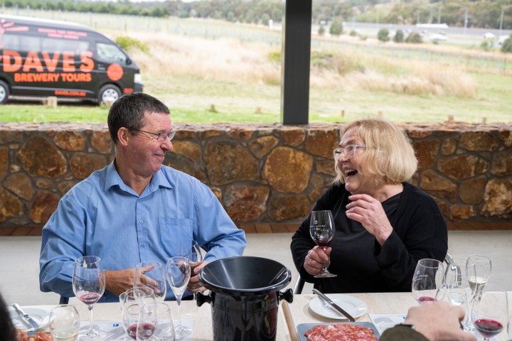 Two people laughing over wine at an outdoor table with a scenic view.