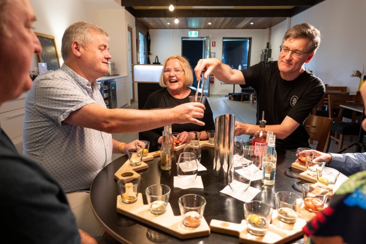 Group of people laughing and mixing drinks around a table.