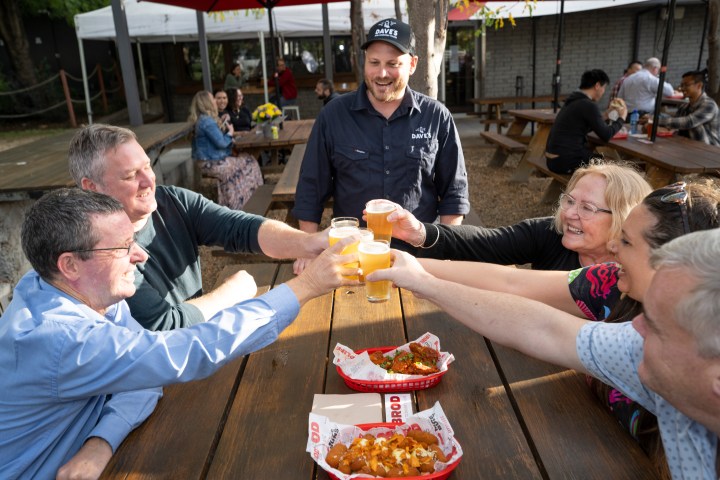 Group of people toasting with beer at an outdoor table with food baskets.