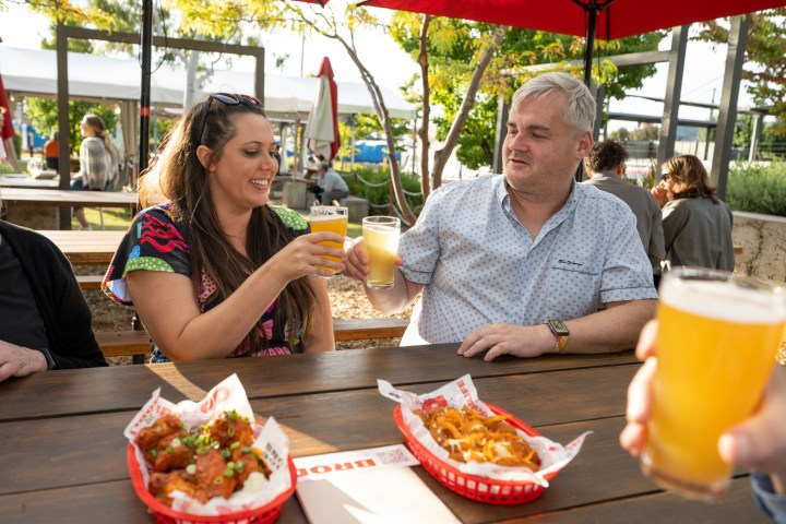 Two people clinking glasses at an outdoor table with food baskets.